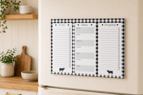 A three-panel kitchen planner magnet set on a cream refrigerator, featuring black and white gingham borders, daily to-do lists, a menu section, and a shopping list with cow illustrations at the bottom.