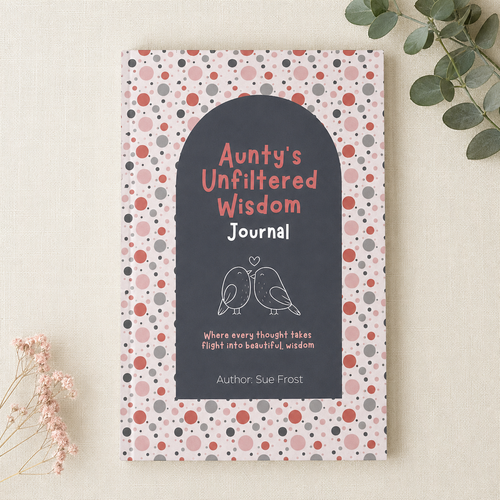 A hardcover journal titled 'Aunty's Unfiltered Wisdom Journal' by Sue Frost, featuring a dark gray arched center with white and pink text and bird illustrations, surrounded by a pink, red, and gray polka dot patterned cover. The book is photographed flat on a light beige textured background with decorative dried flowers and green leaves in the corners.
