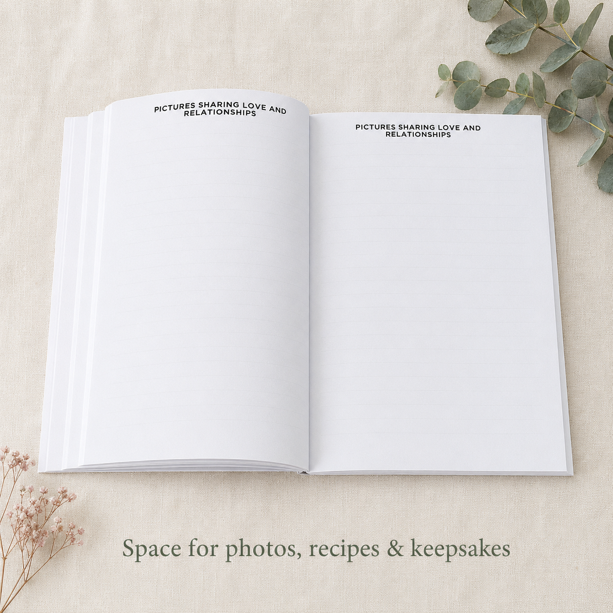 An open white keepsake book or journal laid flat on a light beige fabric surface, with printed text at the top of both pages reading 'PICTURES SHARING LOVE AND RELATIONSHIPS.' Decorative dried flowers and eucalyptus leaves are placed around it, and text at the bottom says 'Space for photos, recipes & keepsakes.
