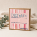 A square kraft gift box with a pink watercolor striped label reading 'Dear Mum' and 'WANDEREFUL GIFT CO', styled on a light beige surface with soft fabric and eucalyptus leaves around it.