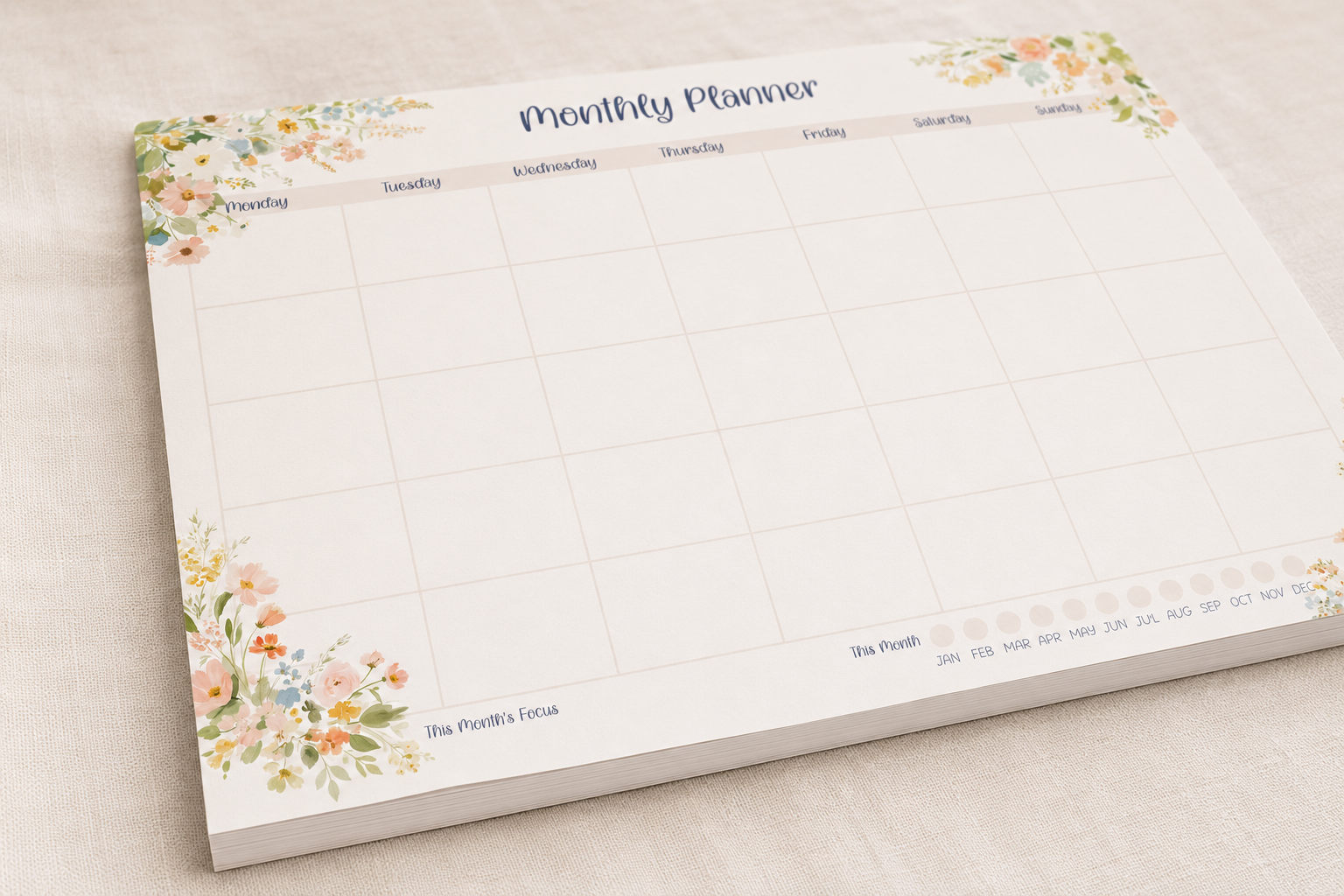 A floral monthly planner pad shown at an angle on a light beige textured surface. The pad features a clean white grid layout with delicate pastel watercolor flowers in the corners and a soft pink header.