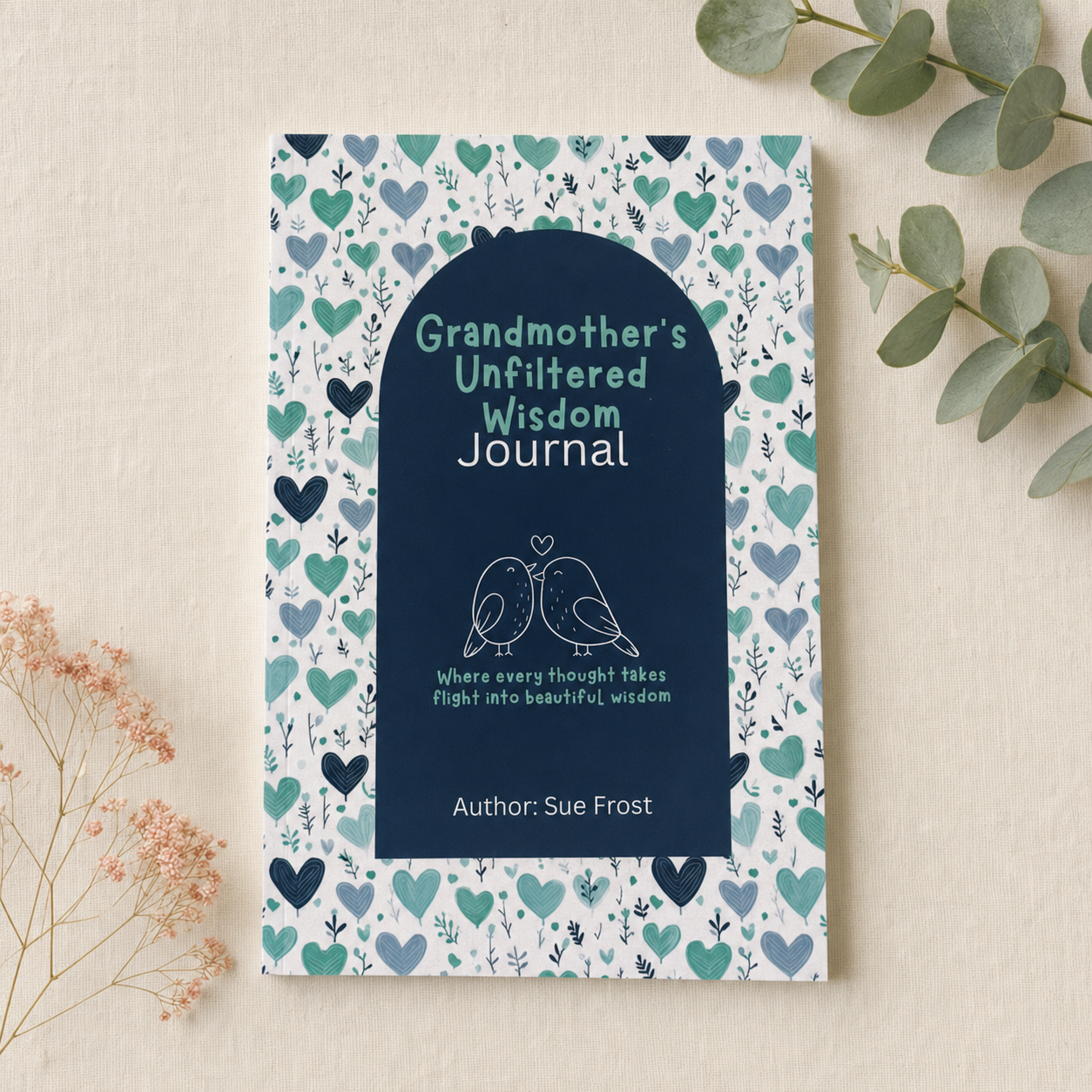 A journal titled 'Grandmother's Unfiltered Wisdom Journal' by Sue Frost, featuring a navy blue cover with a heart pattern border, styled on a beige background with eucalyptus and dried flowers.