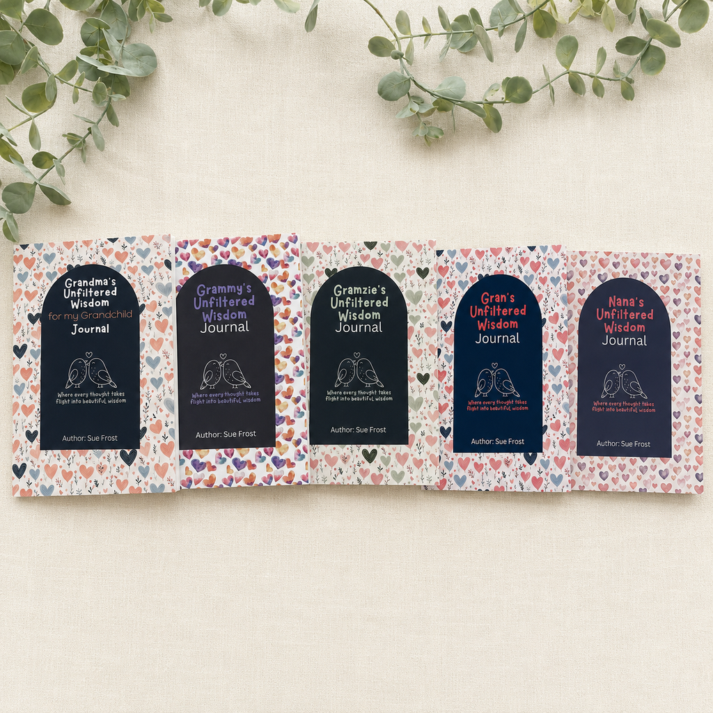 Five folded pages of an unfiltered wisdom journal laid out on a light beige fabric background with green eucalyptus leaves at the top. Each page features a dark navy arch-shaped label with white text reading 'Grandma's Unfiltered Wisdom Journal' and 'Author: Sue Frost, surrounded by a colourful heart pattern. There is 4 other versions with Grammy, Gramzie, Gran and Nana.