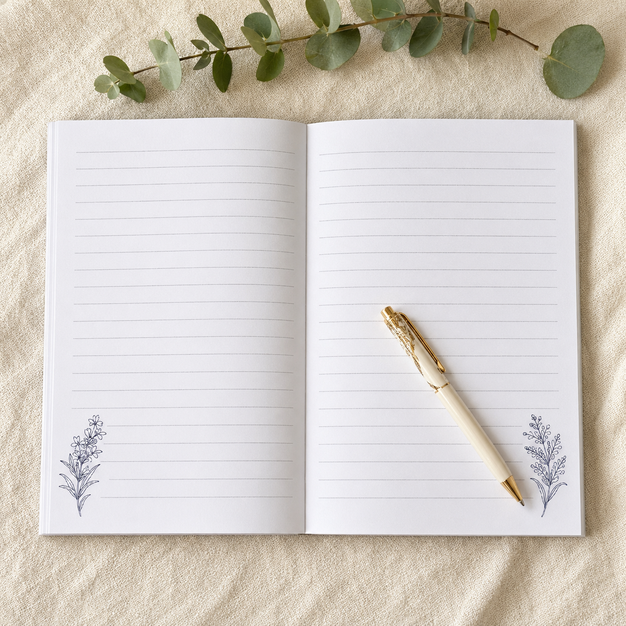 An open lined notebook with two botanical corner illustrations, styled on a beige textured fabric with eucalyptus leaves and a gold pen resting on the pages.