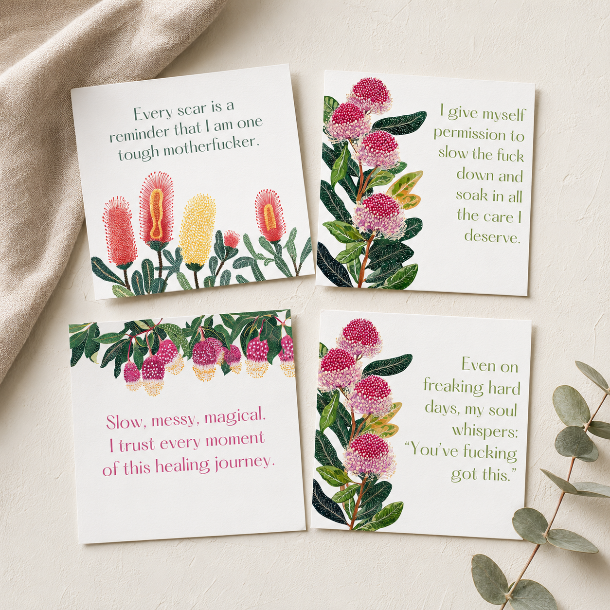 Four square printed cards with floral illustrations and humorous text, arranged on a light beige surface with a draped fabric and eucalyptus stem as props.